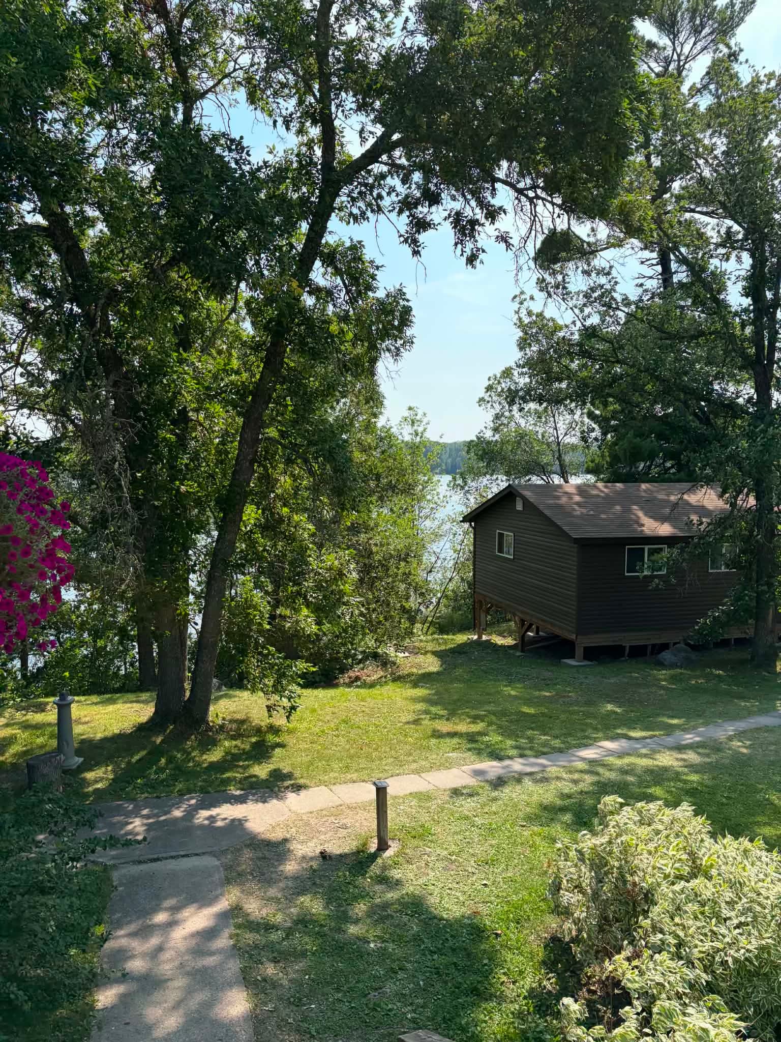 A lakeside cabin surrounded by trees and garden paths at Ash Rapids Lodge